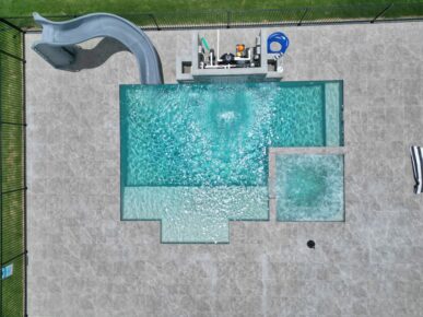 Arialview of a tiled Aqua Technics Saint Remy pool with waterslide, spa zone, and visible filtration system
