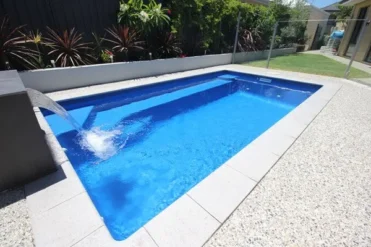 An image of a pool with blue clear water connected with tiled sides and pebble concrete surrounds.