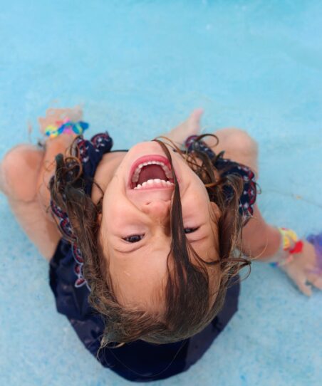 Child with wet hair laughing while sitting in the shallow end of a backyard pool